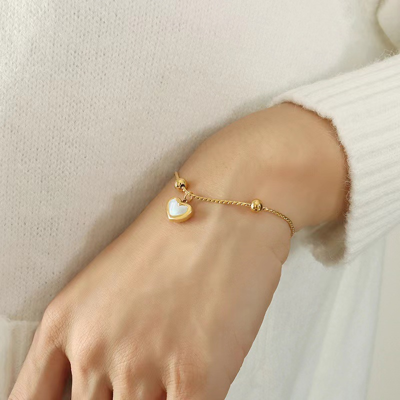 Femme portant un bracelet en acier inoxydable doré coulissant avec charm cœur en nacre
