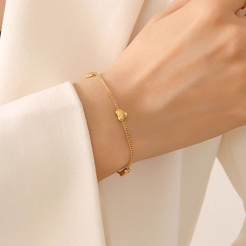 Femme portant un bracelet doré en acier inoxydable, maille gourmette et trois petits cœurs, bijou romantique et ajustable
