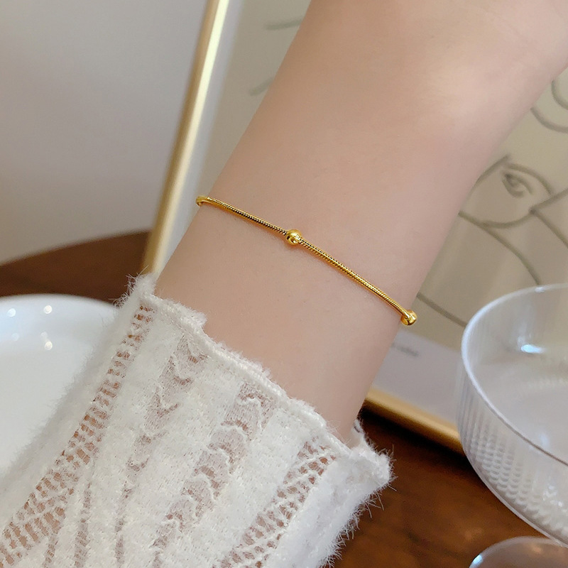 Femme portant un bracelet en acier inoxydable doré, fine maille serpent perlée, style bohème élégant