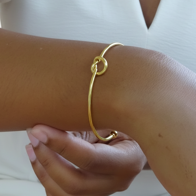 Bracelet manchette fin doré en acier inoxydable, orné d’un cœur noué porté sur un poignet.