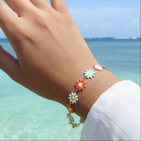 Bracelet en acier inoxydable doré avec petites fleurs marguerite multicolores,  porté sur un poignet.