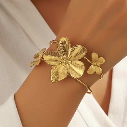 Bracelet manchette en acier inoxydable 316L doré, décoré d’une grande fleur tropicale et de deux papillons, porté sur un poignet.