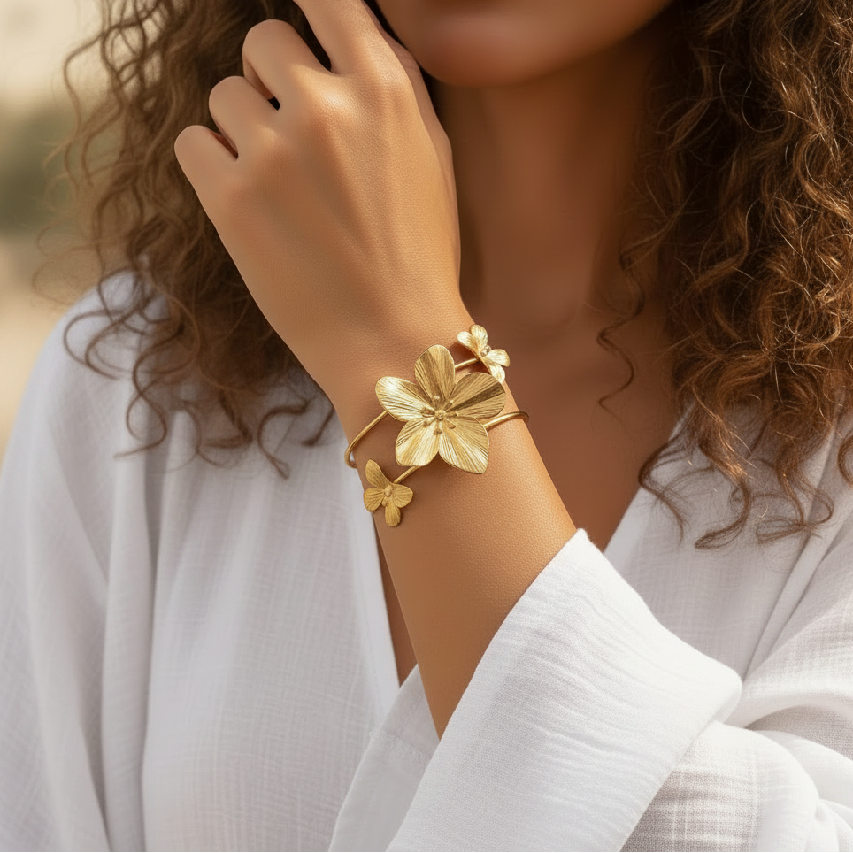Bracelet manchette en acier inoxydable 316L doré, décoré d’une grande fleur tropicale et de deux papillons, porté sur un poignet.