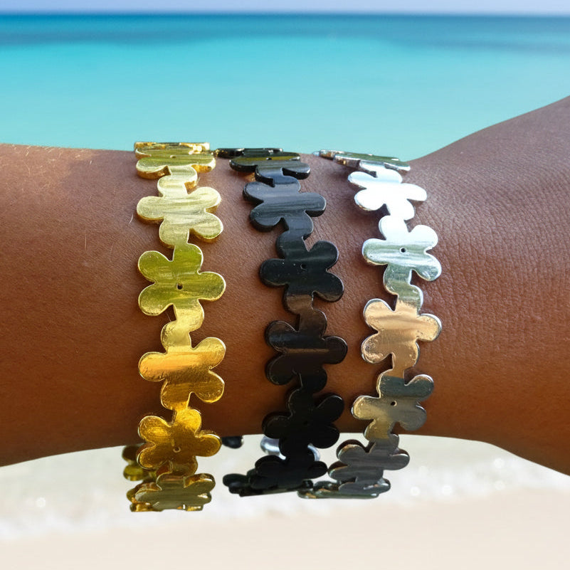Bracelets manchette en acier inoxydable noir, doré et argenté sur le bras d'une femme, petites fleurs décoratives, bijou bohème chic