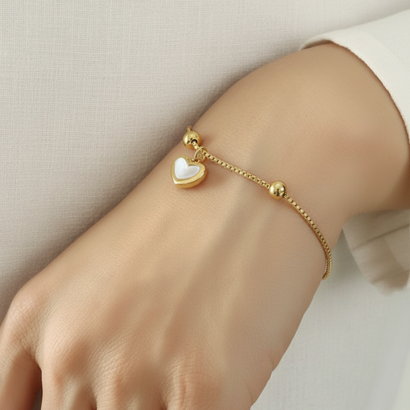 Bracelet fin en acier inoxydable 316L doré avec fermeture coulissante et pendentif cœur en nacre porté sur un poignet.