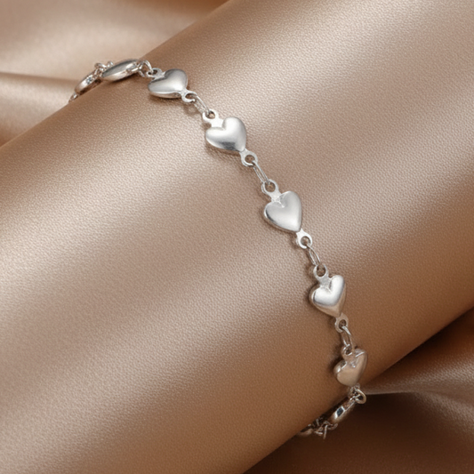 Gros plan sur un bracelet de cheville argenté en acier inoxydable 316L à chaîne ornée de coeurs.