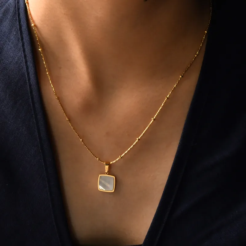 Femme portant un collier doré en acier inoxydable avec pendentif carré en nacre sur fine chaîne à billes et perles dorées