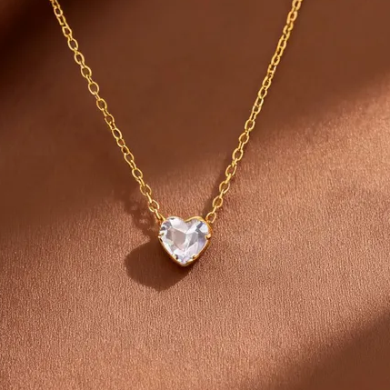 Gros plan sur pendentif coeur en cristal blanc et chaîne fine maille forçat en acier inoxydable 316L doré.