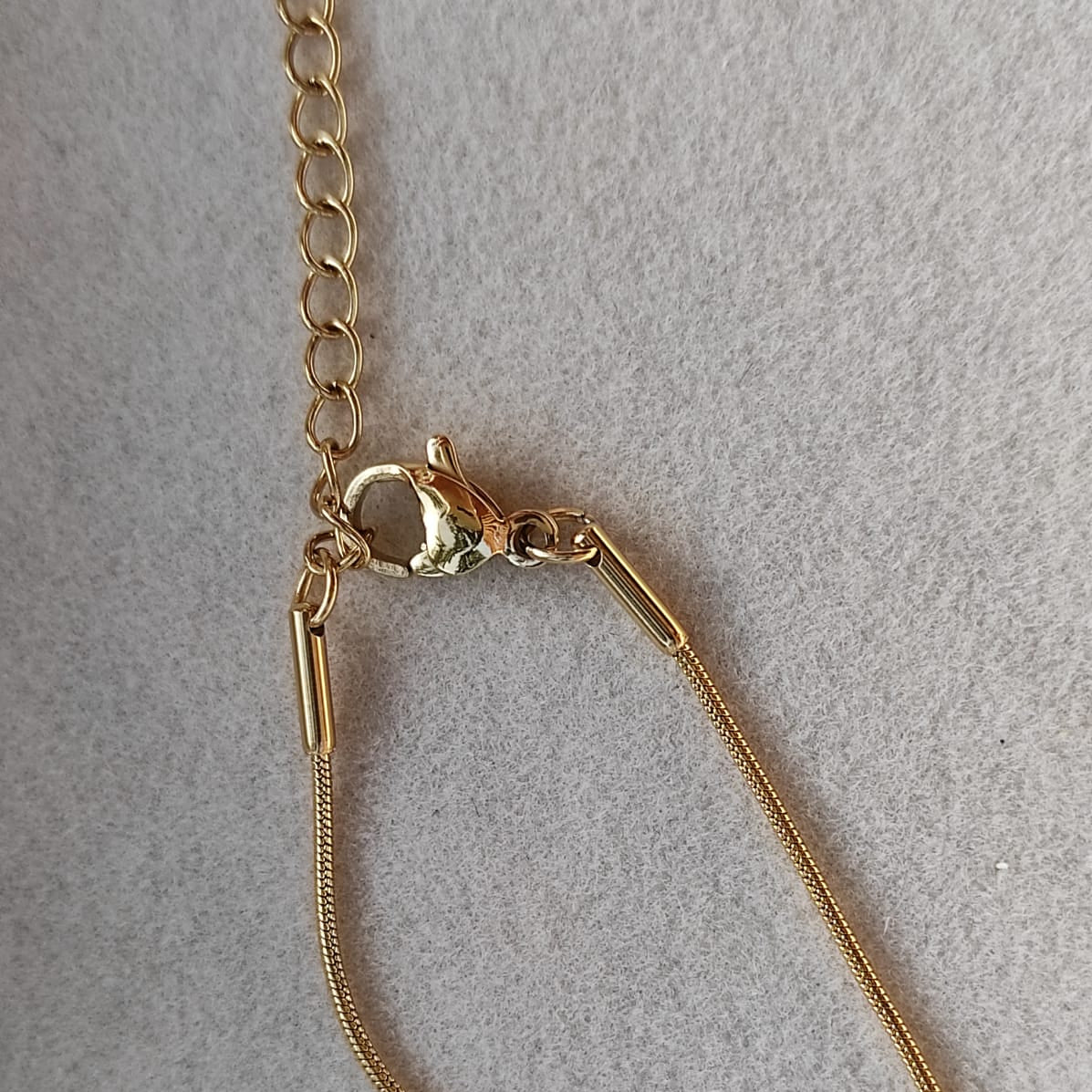 Gros plan sur le fermoir d'un collier doré en acier inoxydable 316L à fine chaîne maille serpent orné d'un cœur en nacre de 1,5 cm.