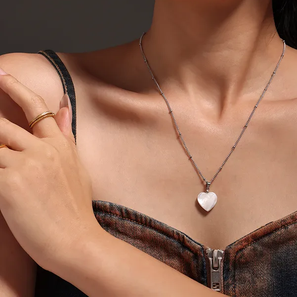 Femme portant un collier argenté en acier inoxydable à maille gourmette perlée orné d’un pendentif cœur en nacre
