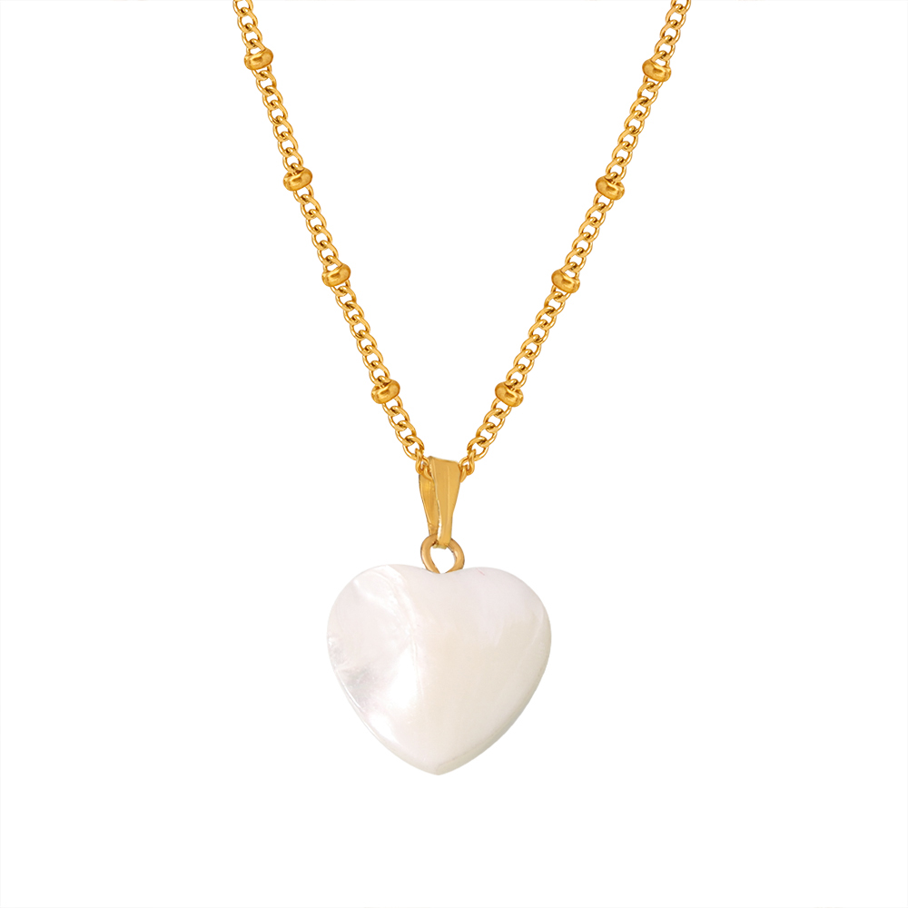 Gros plan sur un collier doré en acier inoxydable à fine chaîne maille gourmette perlée orné d’un pendentif cœur en nacre.
