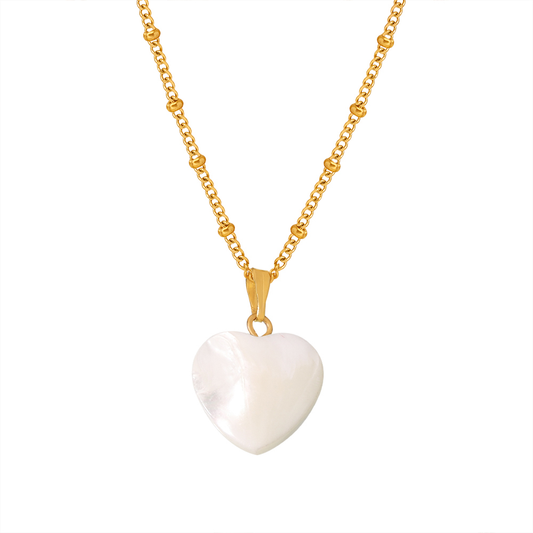 Gros plan sur un collier doré en acier inoxydable à fine chaîne maille gourmette perlée orné d’un pendentif cœur en nacre.