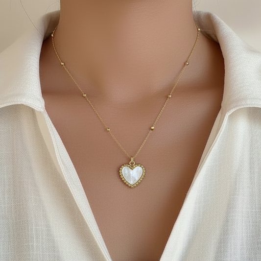 Femme portant un collier doré en acier inoxydable avec fine chaîne forçat perlée et pendentif coeur en nacre, style bohème