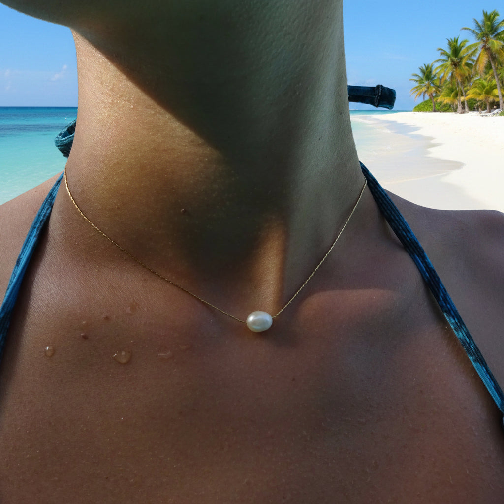 Collier en acier inoxydable 316L doré à chaîne ultra fine orné d'une perle d’eau douce blanche porté par une femme.