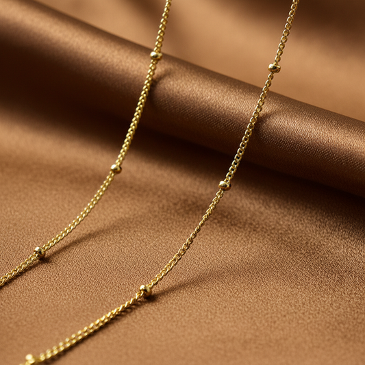Gros plan sur un collier doré en acier inoxydable à chaîne fine maille gourmette et perles dorées.