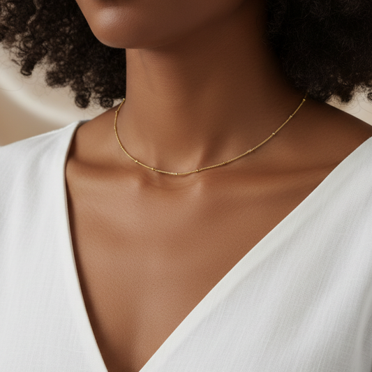 Femme portant un collier doré en acier inoxydable à chaîne fine maille gourmette et perles dorées.