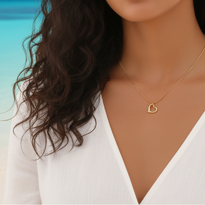 Femme portant un collier doré en acier inoxydable 316L à fine chaîne maille serpent orné d'un pendentif petit cœur ajouré stylisé.