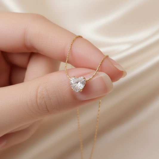 Collier femme avec pendentif petit coeur en zirconium blanc et chaîne ultra fine maille bambou en acier inoxydable 316L doré, bijou délicat, élégant et intemporel exposé sur un doigt