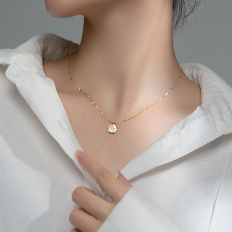 Femme portant un collier doré en acier inoxydable avec fine maille forçat et pendentif carré en nacre