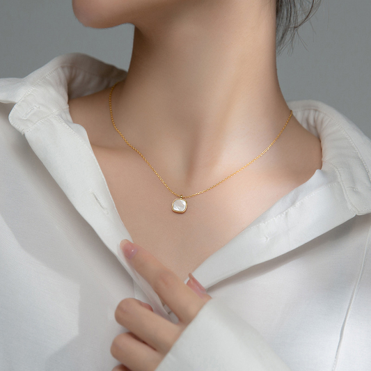 Femme portant un collier doré en acier inoxydable avec fine maille forçat et pendentif carré en nacre