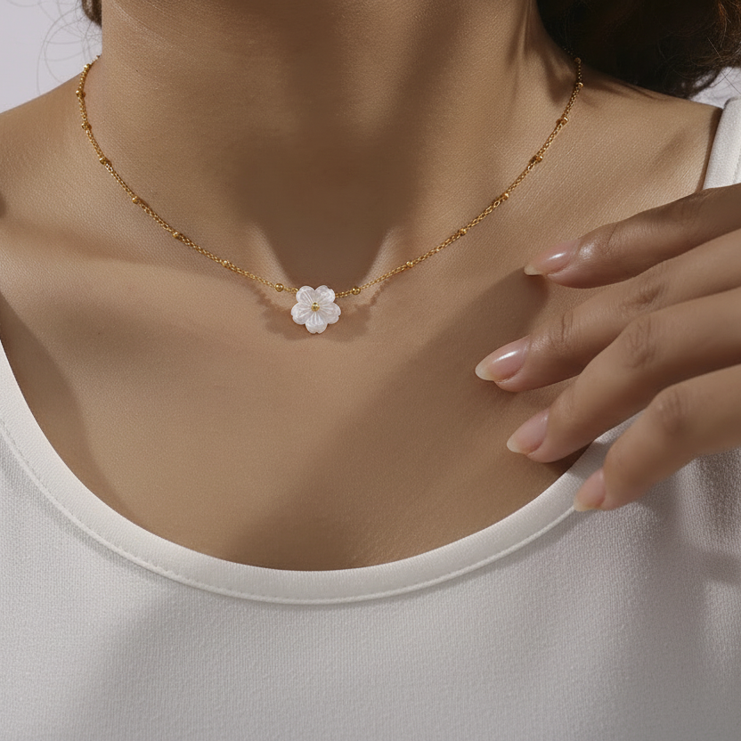 Femme portant un collier doré en acier inoxydable à fine maille forçat perlée orné d'un pendentif fleur en nacre.