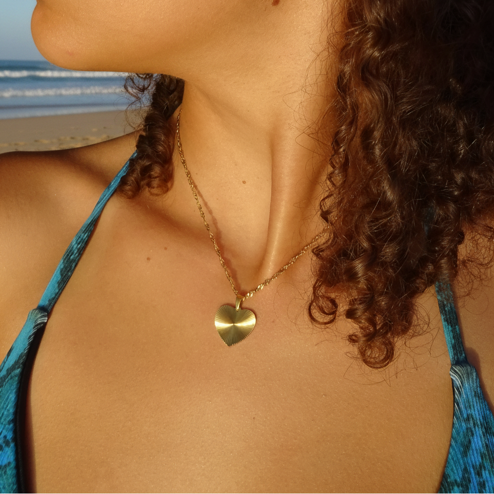 Collier doré en acier inoxydable 316L à chaîne maille torsadée avec pendentif cœur stylisé porté par une femme.