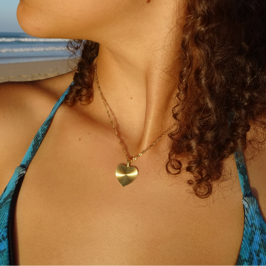 Collier doré en acier inoxydable 316L à chaîne maille torsadée avec pendentif cœur stylisé porté par une femme.