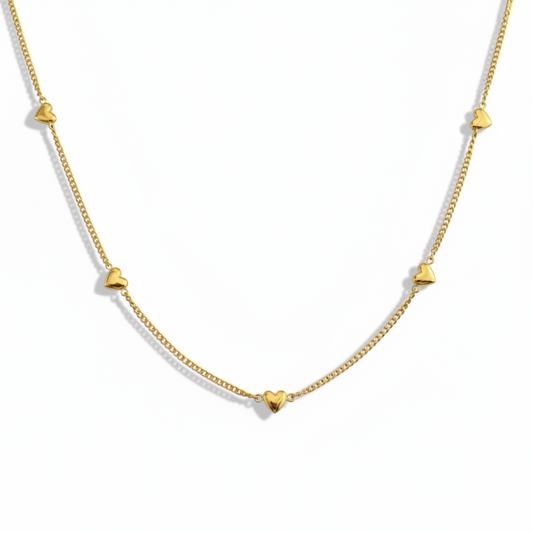 Gros plan sur un collier doré en acier inoxydable 316L à fine maille gourmette orné de neuf petits cœurs.
