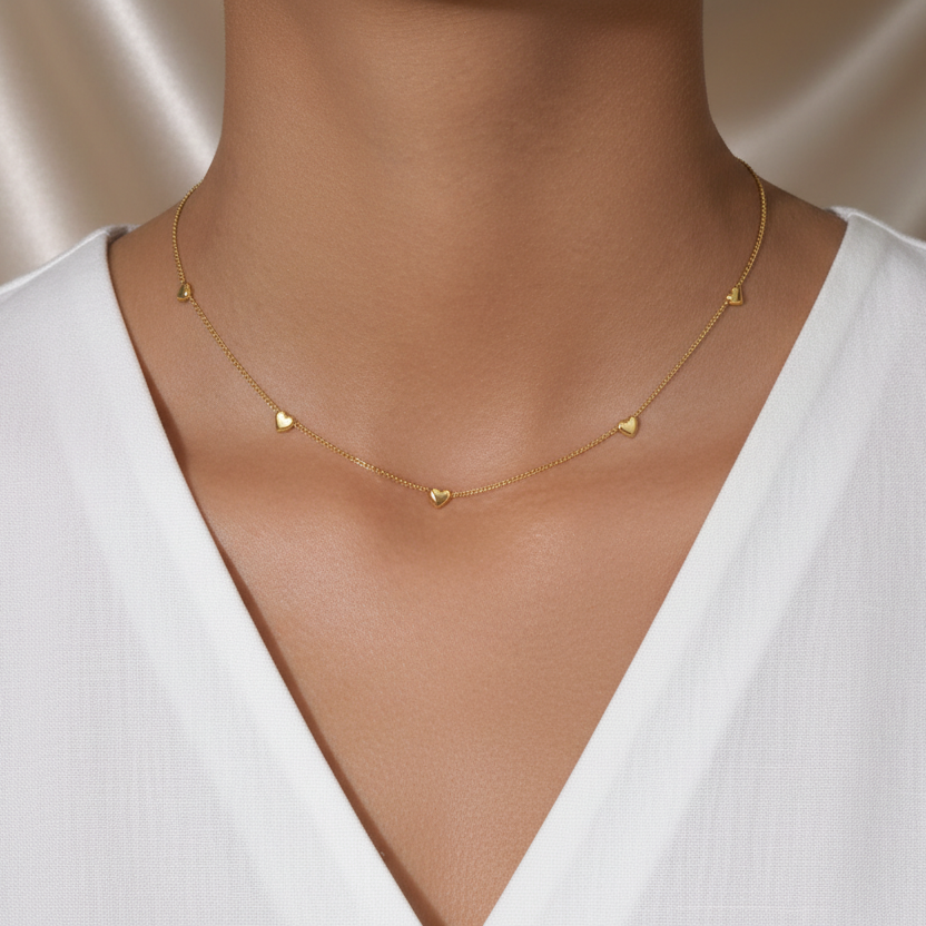 Femme portant un collier doré en acier inoxydable 316L à fine maille gourmette orné de neuf petits cœurs.