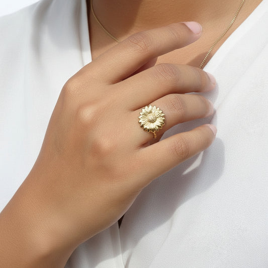 Main portant une bague ajustable en acier inoxydable doré, ornée d'une fleur marguerite.