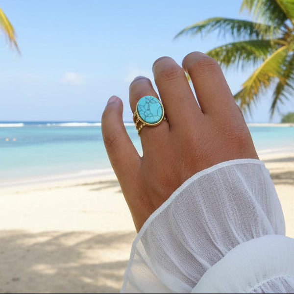 Main de femme portant une bague dorée en acier inoxydable ornée d'une pierre naturelle turquoise.