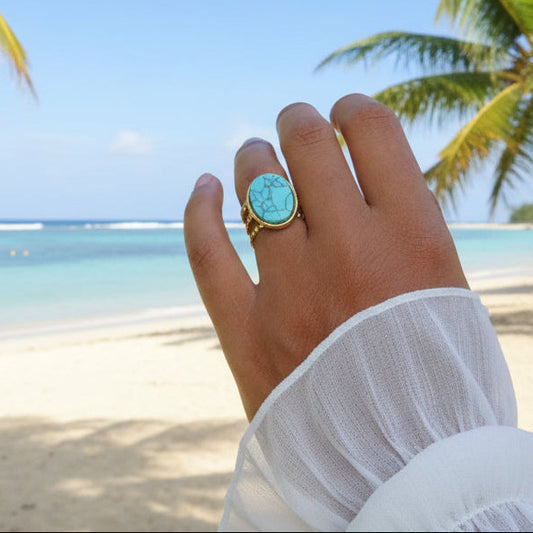 Main de femme portant une bague dorée en acier inoxydable ornée d'une pierre naturelle turquoise.