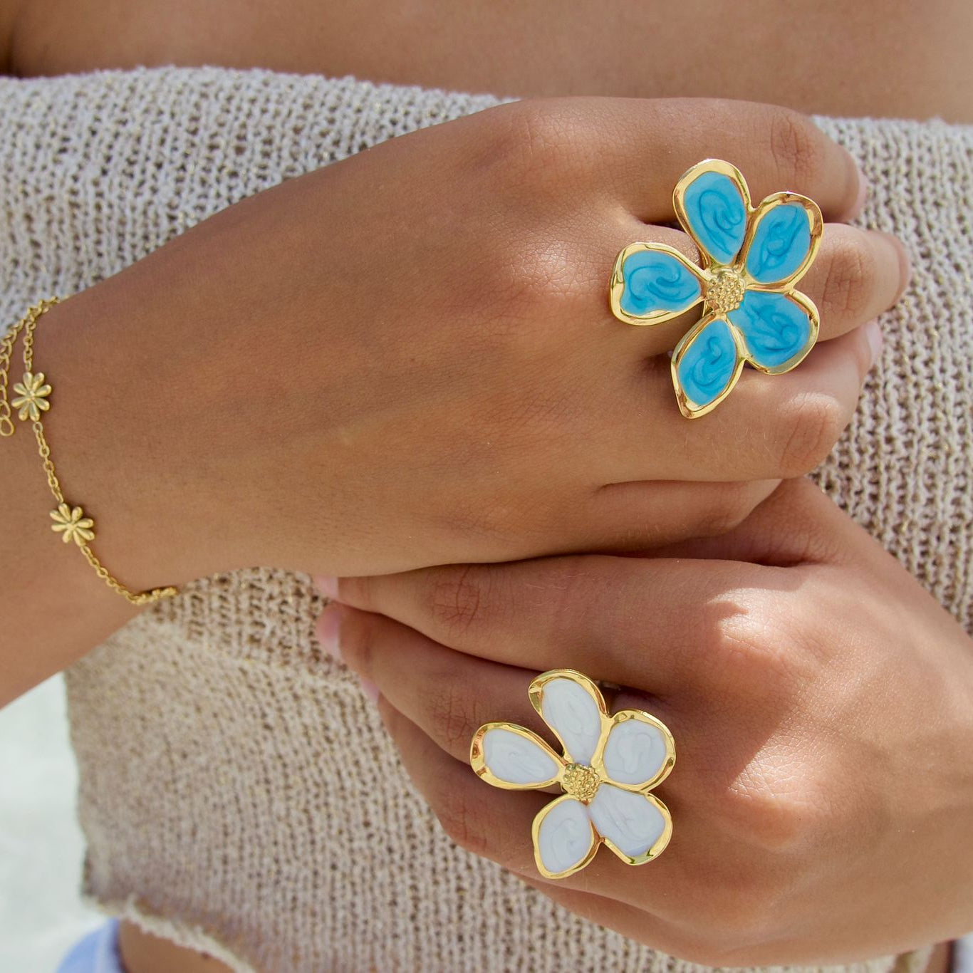 Femme portant des bagues dorées ajustables en acier inoxydable, ornées d’une fleur en émail, disponible en bleu, rose, rouge et blanc.