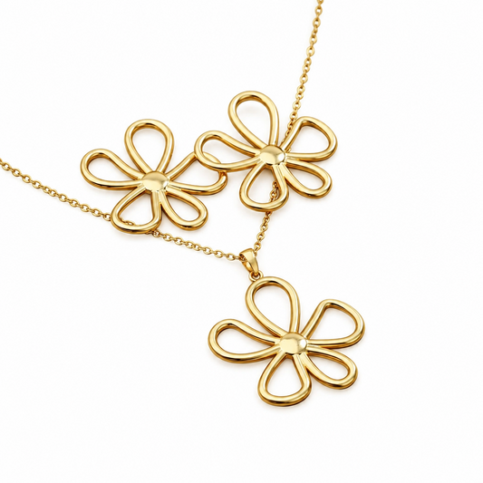 Parure grande fleur ajourée comprenant un collier et des boucles d'oreilles en acier inoxydable doré sur fond banc.