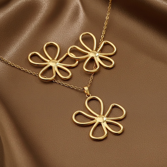 Parure grande fleur ajourée comprenant un collier et des boucles d'oreilles en acier inoxydable doré sur fond satin.
